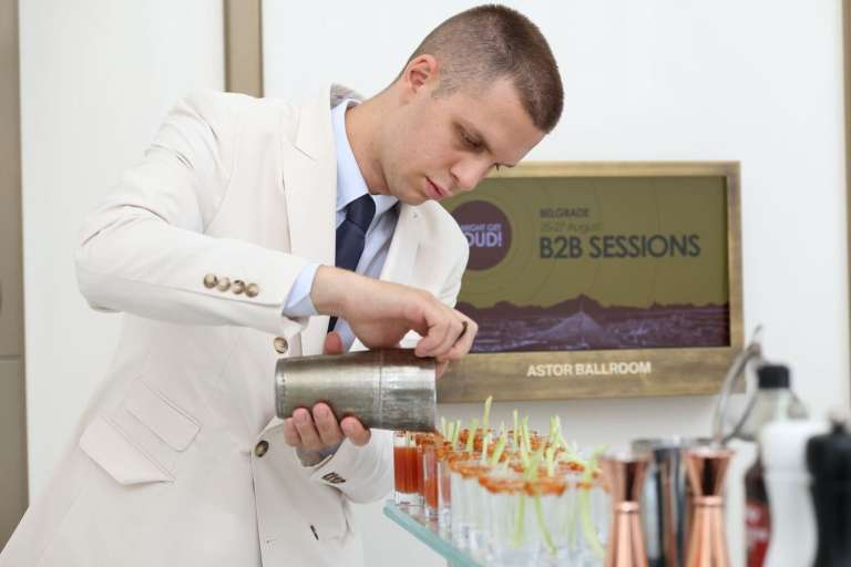 A bartender preparing cocktails next to an info screen announcing the IMGL 2026 B2B sessions