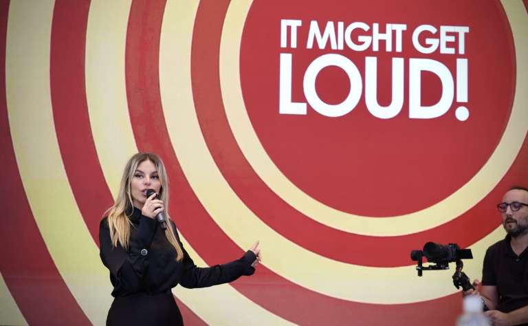 Master of ceremony holding a microphone in front of a branded event background during IMGL 2026.
