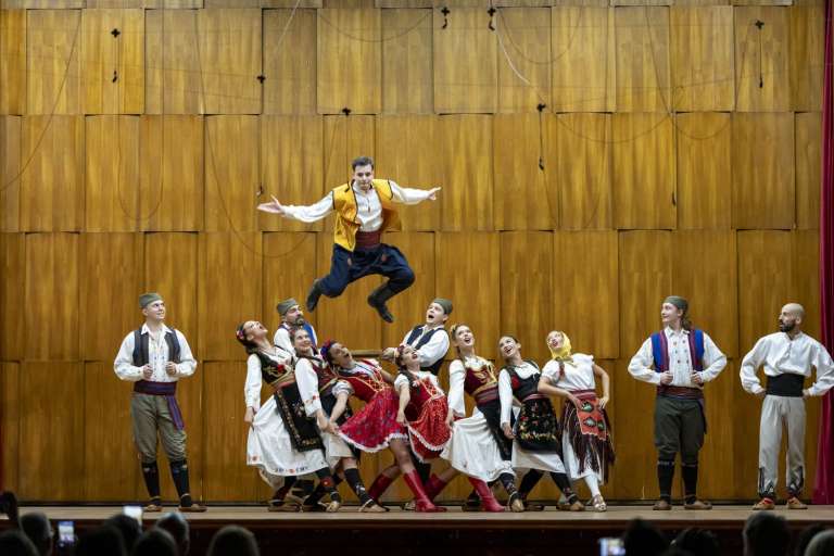 Performers in traditional Serbian folk costumes mid-dance on stage at the Kolarac concert hall during the IMGL 2026 cultural evening
